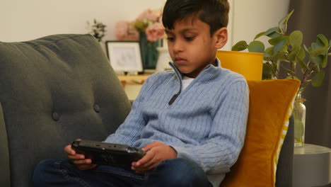 Young-Boy-Sitting-On-Sofa-At-Home-Playing-Game-Or-Streaming-Onto-Handheld-Gaming-Device-2